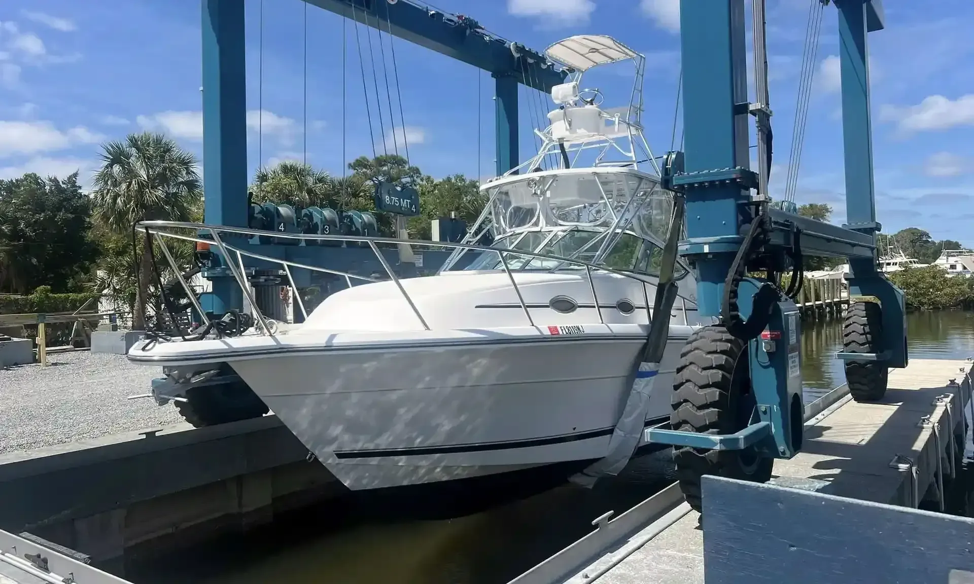A white sportfishing boat lifted out of the water in a marina travel lift.