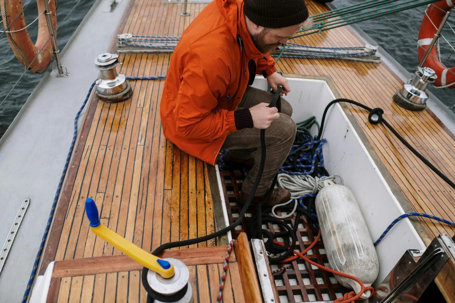 A technician in an orange jacket handling a line on the teak deck of a boat.